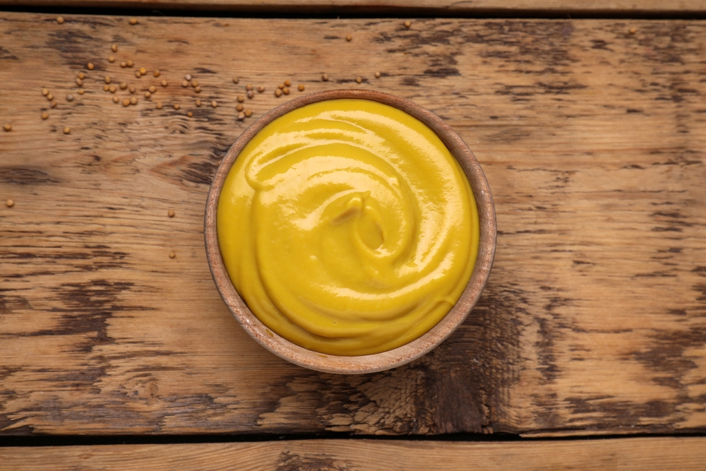 Sauce bowl with delicious mustard and seeds on wooden table