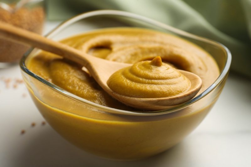 Spoon and glass bowl with tasty mustard sauce on white table