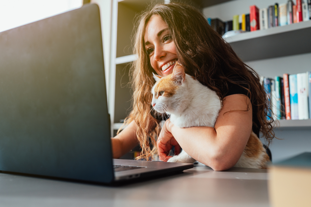 young woman owner using laptop with her pet cat